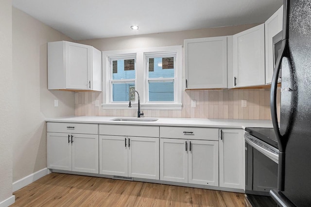 kitchen with range with electric cooktop, black fridge, sink, white cabinetry, and backsplash