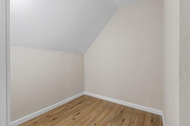 additional living space with wood-type flooring and vaulted ceiling