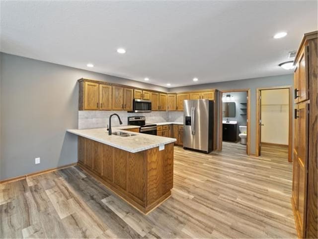 kitchen with kitchen peninsula, light wood-type flooring, backsplash, appliances with stainless steel finishes, and sink