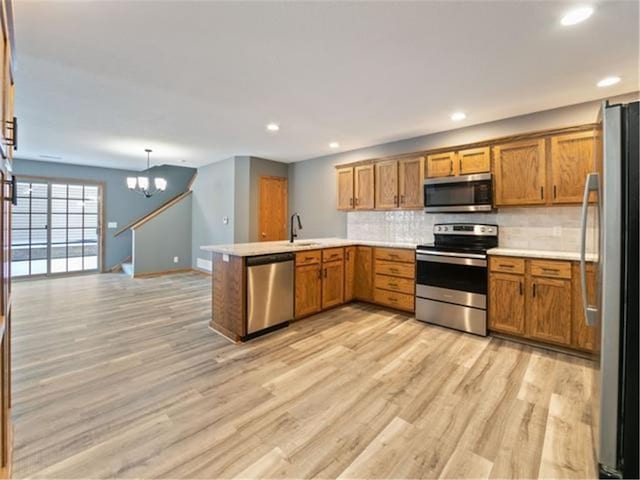 kitchen featuring light hardwood / wood-style flooring, kitchen peninsula, a chandelier, pendant lighting, and appliances with stainless steel finishes