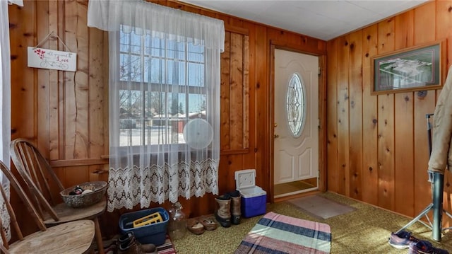 doorway to outside with carpet floors, wood walls, and plenty of natural light