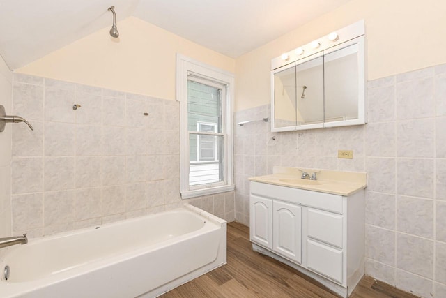 bathroom with vaulted ceiling, hardwood / wood-style floors, tile walls, a bathing tub, and vanity