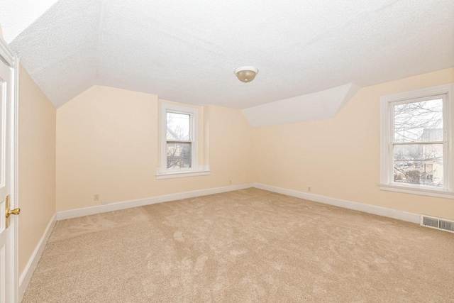 bonus room with a textured ceiling, vaulted ceiling, and light carpet