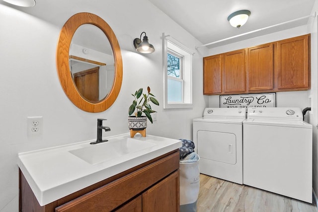 clothes washing area featuring washing machine and dryer, cabinets, light hardwood / wood-style flooring, and sink