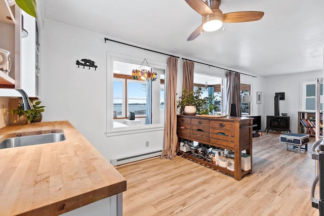 kitchen featuring sink, a wood stove, light hardwood / wood-style flooring, ceiling fan with notable chandelier, and a baseboard radiator