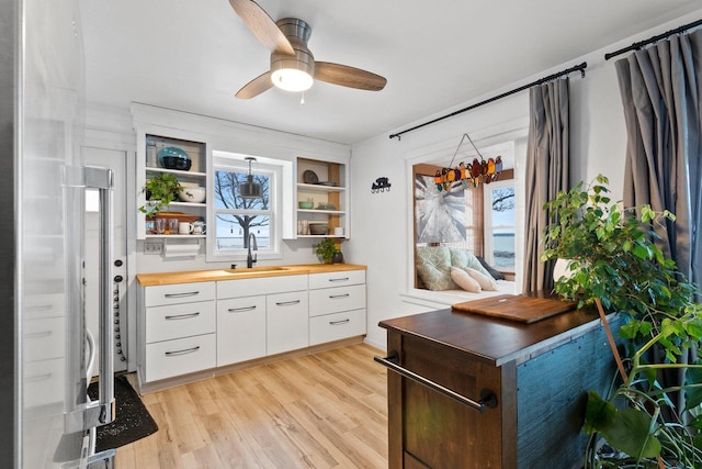 kitchen with light hardwood / wood-style flooring, butcher block countertops, white cabinets, ceiling fan, and sink