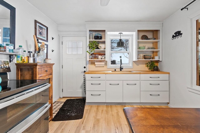 kitchen with sink, white cabinetry, wood counters, range with two ovens, and pendant lighting