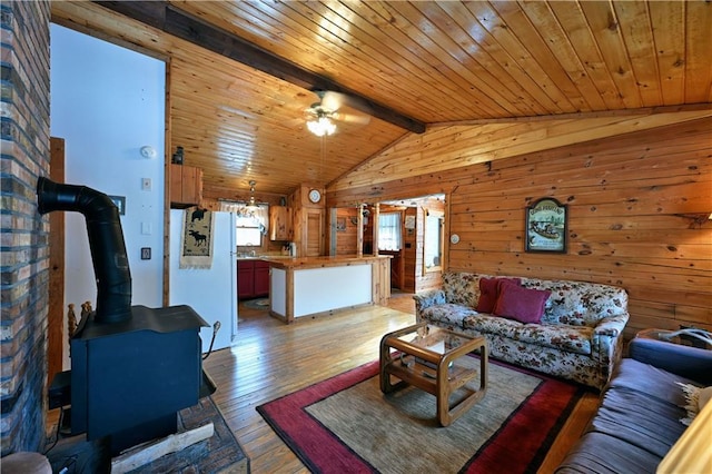 living room featuring a wood stove, ceiling fan, hardwood / wood-style floors, wood walls, and lofted ceiling with beams