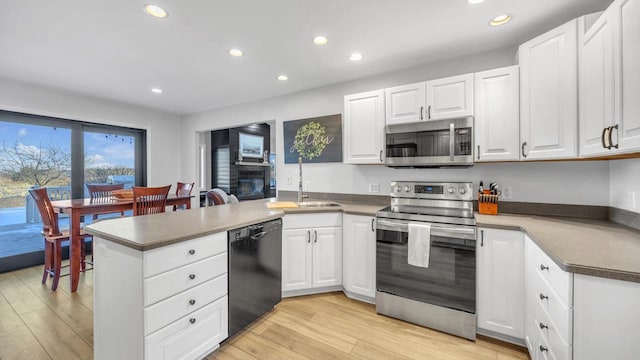 kitchen featuring stainless steel appliances, sink, white cabinetry, light hardwood / wood-style floors, and kitchen peninsula