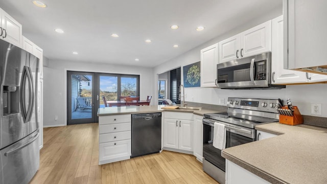 kitchen with stainless steel appliances, light wood-type flooring, kitchen peninsula, white cabinets, and sink