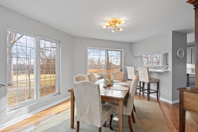 dining space with sink, light hardwood / wood-style floors, plenty of natural light, and a notable chandelier