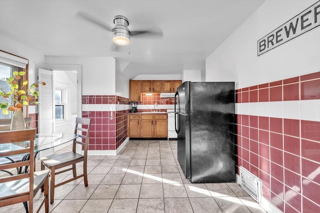 kitchen featuring black refrigerator, light tile patterned floors, tile walls, ceiling fan, and sink