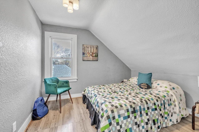 bedroom with lofted ceiling, light wood-type flooring, and a textured ceiling