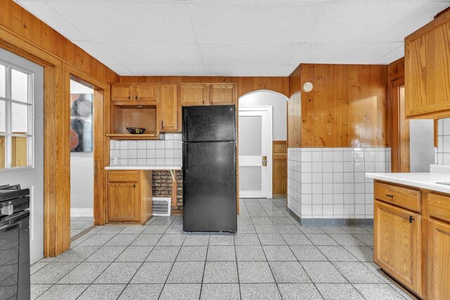 kitchen with a drop ceiling, wooden walls, and black refrigerator