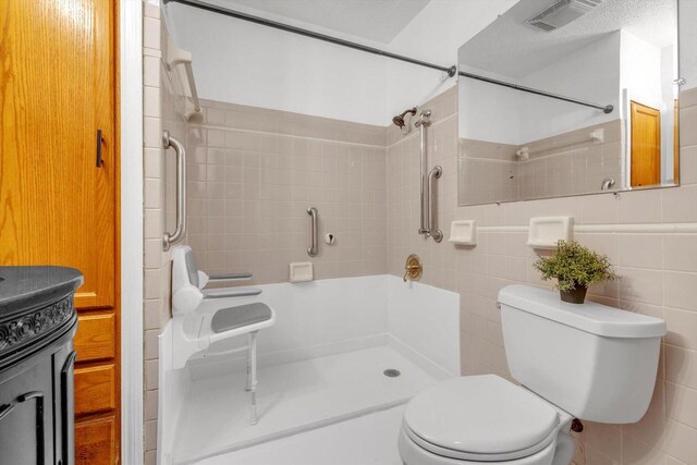 bathroom featuring toilet, vanity, tile walls, a tile shower, and a textured ceiling