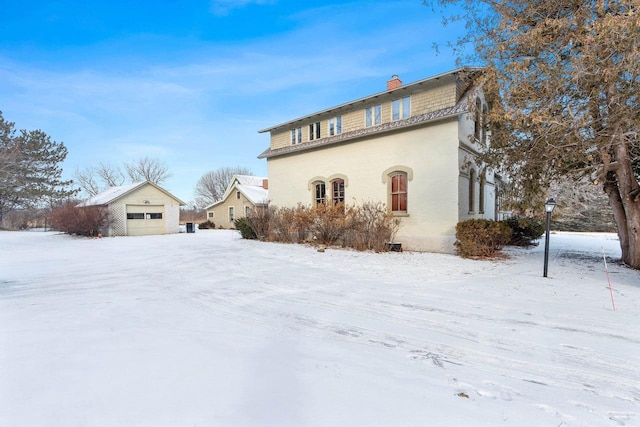 snow covered property with a garage and an outbuilding