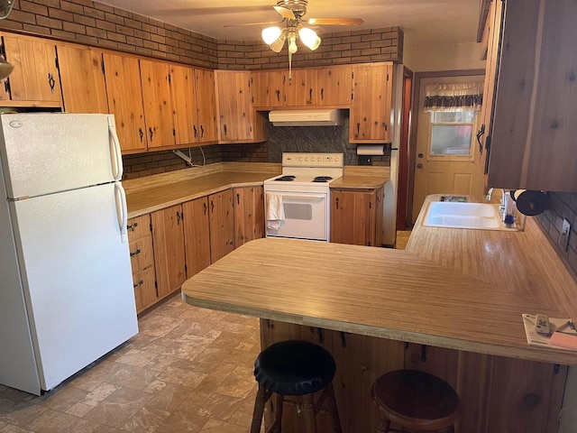 kitchen with white appliances, kitchen peninsula, ceiling fan, a breakfast bar, and sink