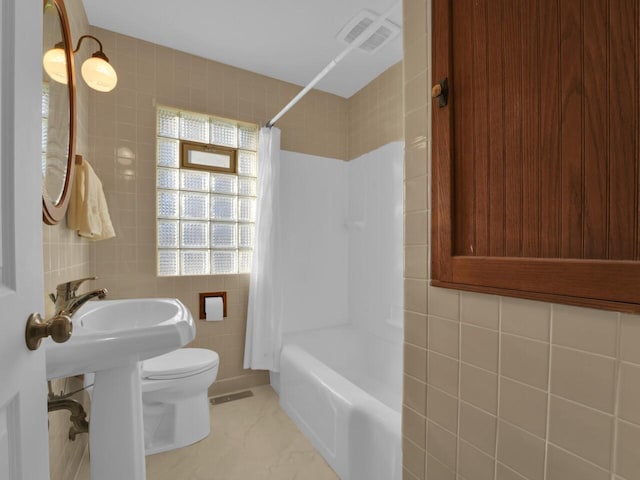 bathroom featuring tile walls, shower / bath combination with curtain, and toilet