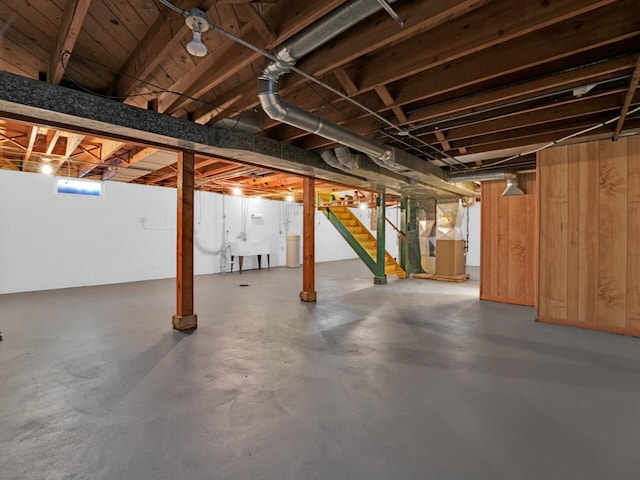 basement featuring wood walls, heating unit, and sink