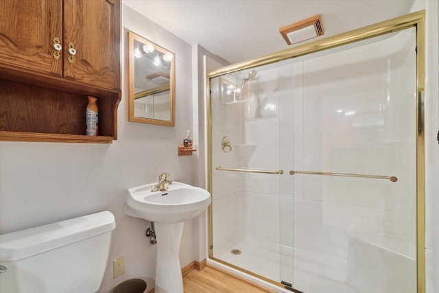 bathroom with toilet, a shower with door, and wood-type flooring