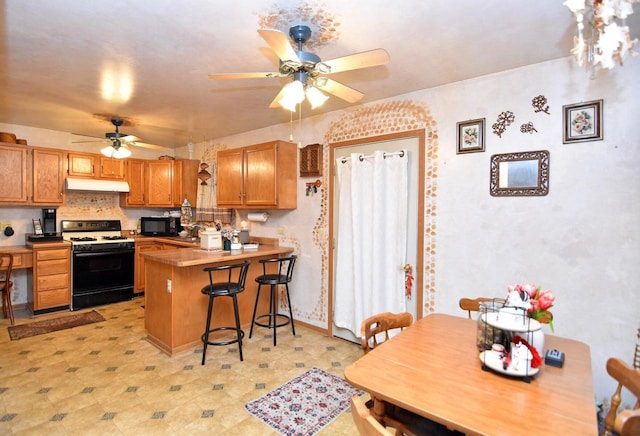 kitchen featuring ceiling fan, a kitchen bar, gas stove, and kitchen peninsula