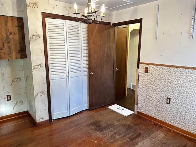 unfurnished bedroom with dark wood-type flooring and an inviting chandelier