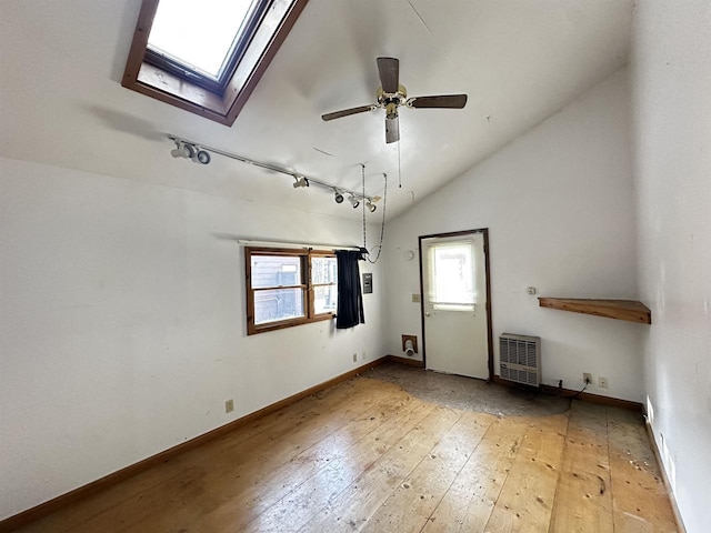 unfurnished room featuring track lighting, lofted ceiling with skylight, light wood-type flooring, heating unit, and ceiling fan