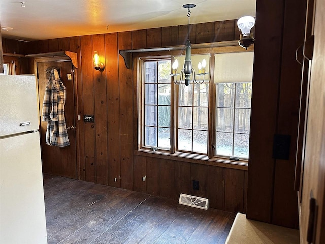 unfurnished dining area featuring a notable chandelier, dark hardwood / wood-style flooring, and wooden walls