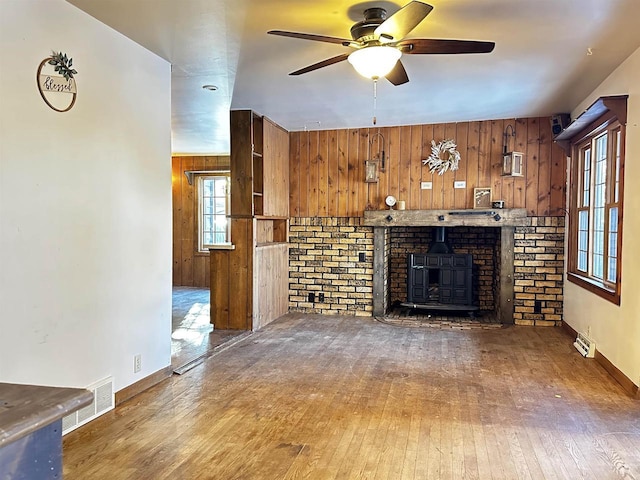 unfurnished living room with dark hardwood / wood-style flooring, wooden walls, ceiling fan, and a wood stove