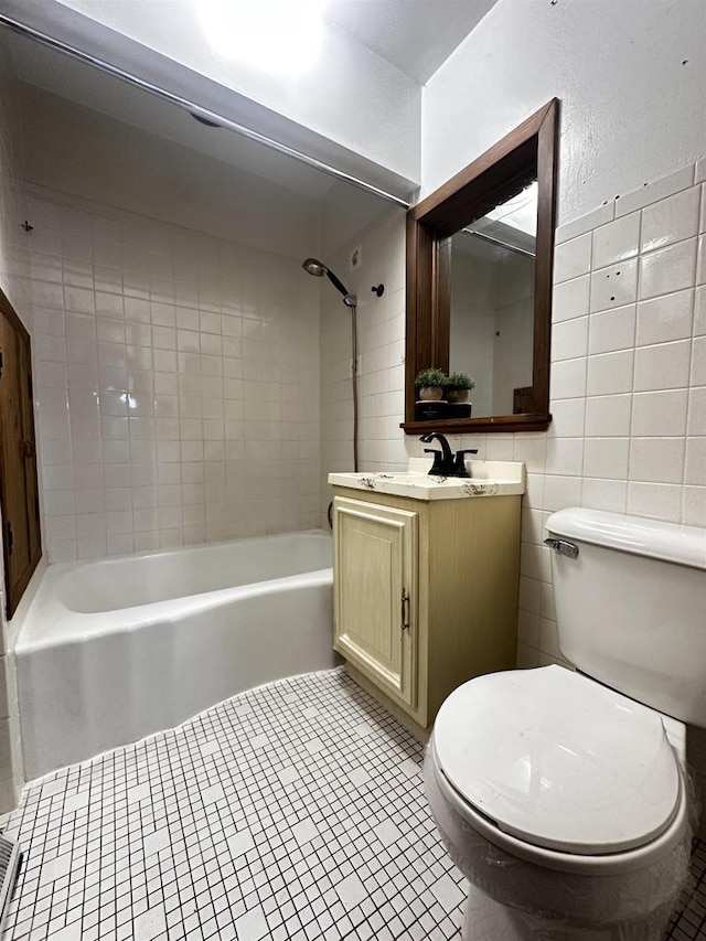 full bathroom with tiled shower / bath, tile walls, toilet, tile patterned floors, and vanity