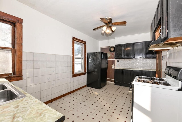 kitchen with sink, white gas stove, black fridge, tile walls, and ceiling fan