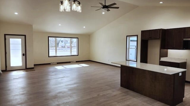 kitchen featuring a kitchen island, light hardwood / wood-style floors, ceiling fan with notable chandelier, high vaulted ceiling, and pendant lighting