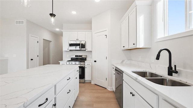 kitchen featuring appliances with stainless steel finishes, hanging light fixtures, light stone counters, white cabinets, and sink