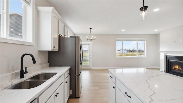 kitchen featuring sink, white cabinetry, decorative light fixtures, and light stone counters