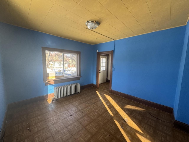 empty room featuring dark parquet flooring and radiator heating unit