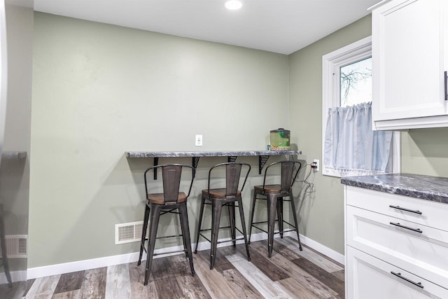 kitchen with a breakfast bar, light hardwood / wood-style flooring, and white cabinetry