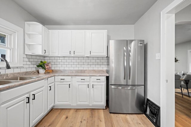 kitchen featuring decorative backsplash, light wood-type flooring, white cabinetry, stainless steel refrigerator, and sink