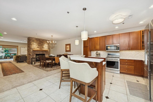 kitchen with a kitchen breakfast bar, appliances with stainless steel finishes, light colored carpet, an island with sink, and pendant lighting