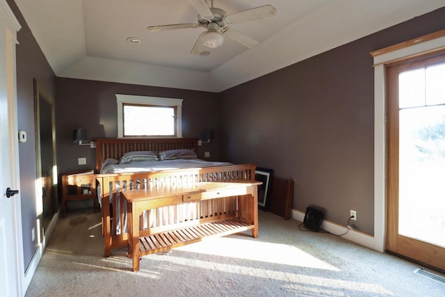 carpeted bedroom featuring vaulted ceiling, ceiling fan, a tray ceiling, and multiple windows