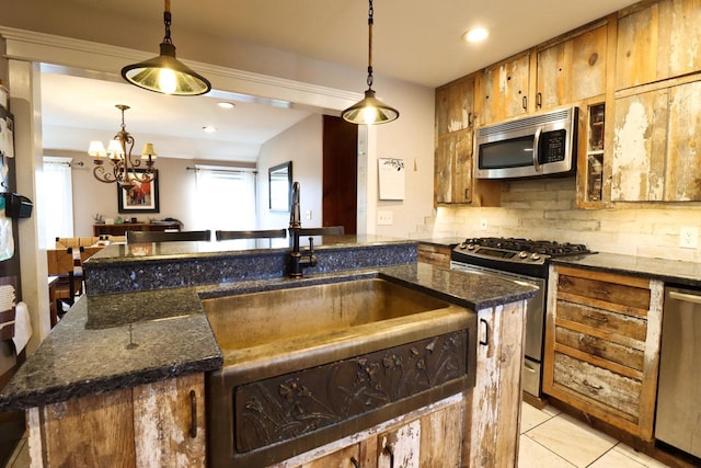 kitchen featuring dark stone countertops, a center island with sink, stainless steel appliances, decorative light fixtures, and tasteful backsplash