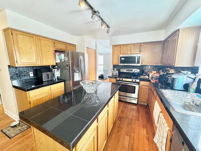 kitchen featuring stainless steel appliances, decorative backsplash, a kitchen island, sink, and light hardwood / wood-style flooring