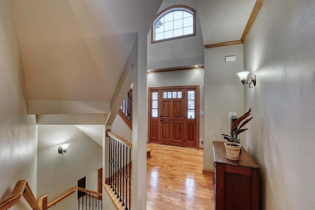 entryway featuring a towering ceiling, light hardwood / wood-style floors, and crown molding