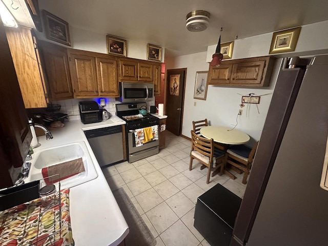 kitchen with appliances with stainless steel finishes, sink, light tile patterned floors, and decorative backsplash