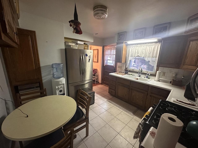 kitchen with sink, gas range, light tile patterned floors, stainless steel fridge, and backsplash