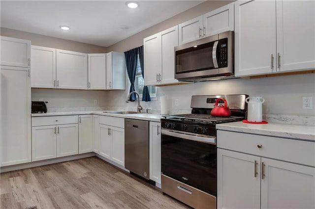 kitchen featuring stainless steel appliances, light stone counters, sink, light hardwood / wood-style flooring, and white cabinetry