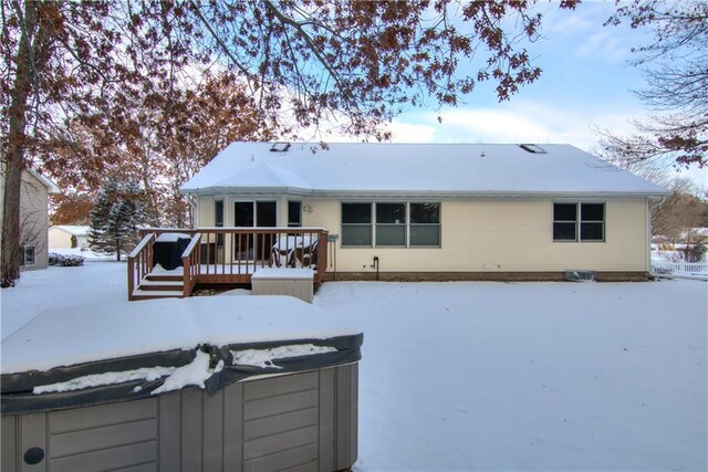 snow covered back of property featuring a deck and a hot tub