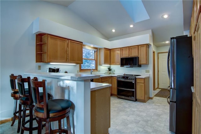 kitchen featuring black fridge, lofted ceiling with skylight, a kitchen breakfast bar, kitchen peninsula, and double oven range