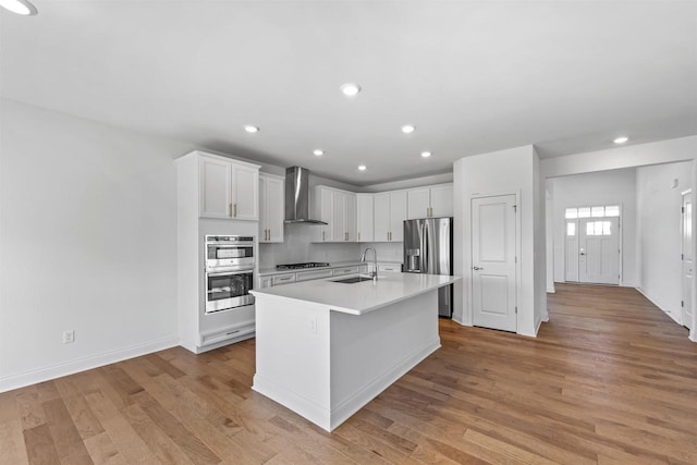 kitchen with sink, white cabinetry, wall chimney exhaust hood, an island with sink, and appliances with stainless steel finishes