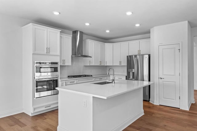 kitchen featuring an island with sink, wall chimney exhaust hood, white cabinets, and sink