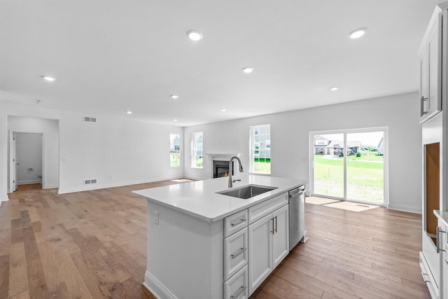 kitchen featuring stainless steel dishwasher, light hardwood / wood-style floors, a kitchen island with sink, white cabinetry, and sink